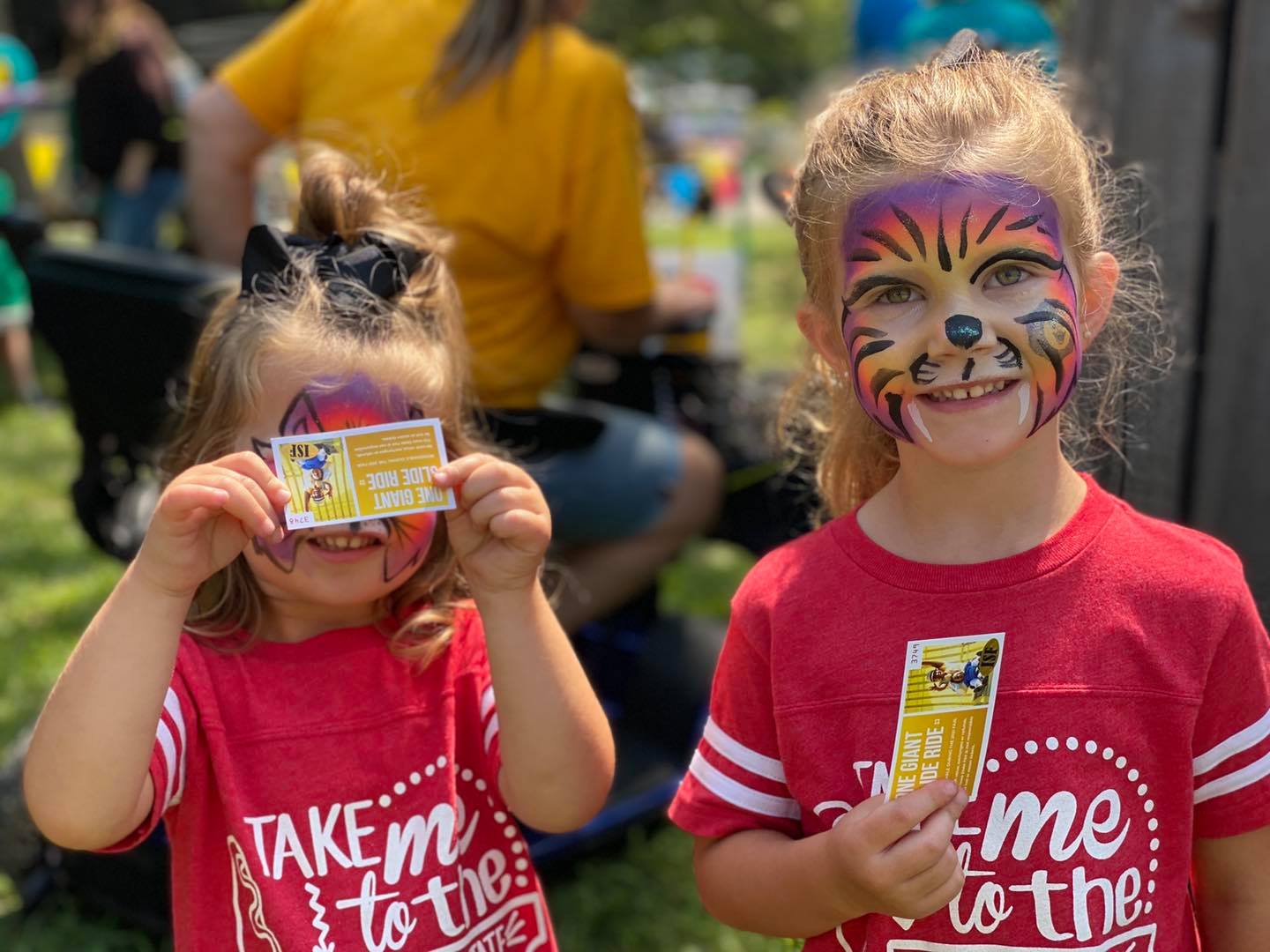 Two children stand holding tickets with their faces painted like purple tigers.