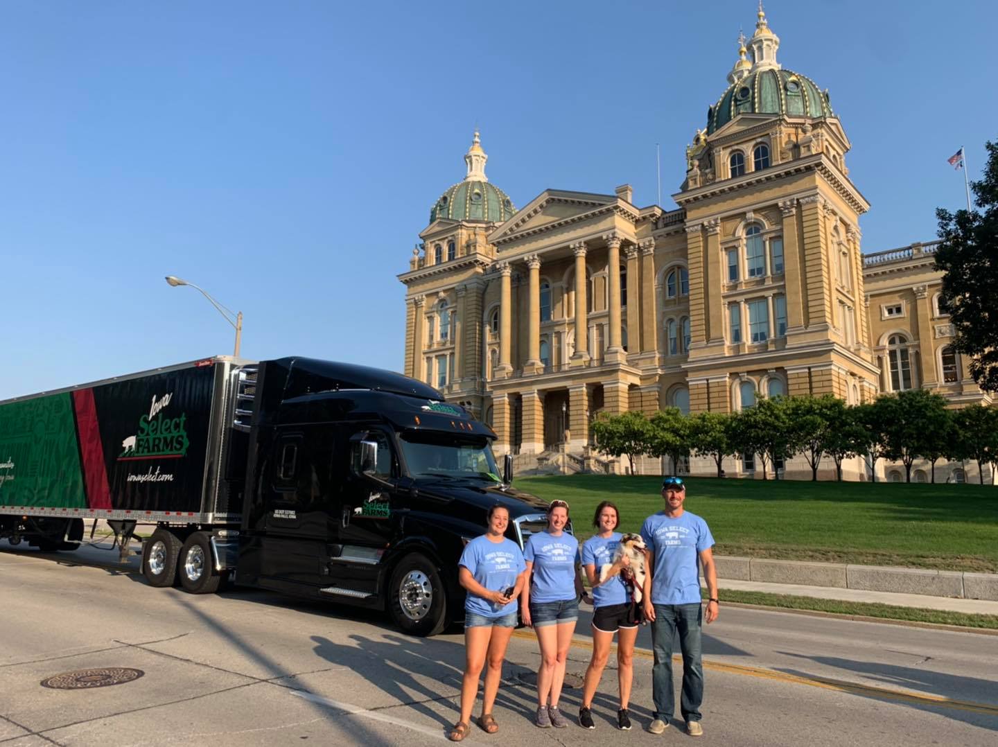 A group of parade volunteers stand in front of the Iowa State Capitol and an Iowa Select semi.
