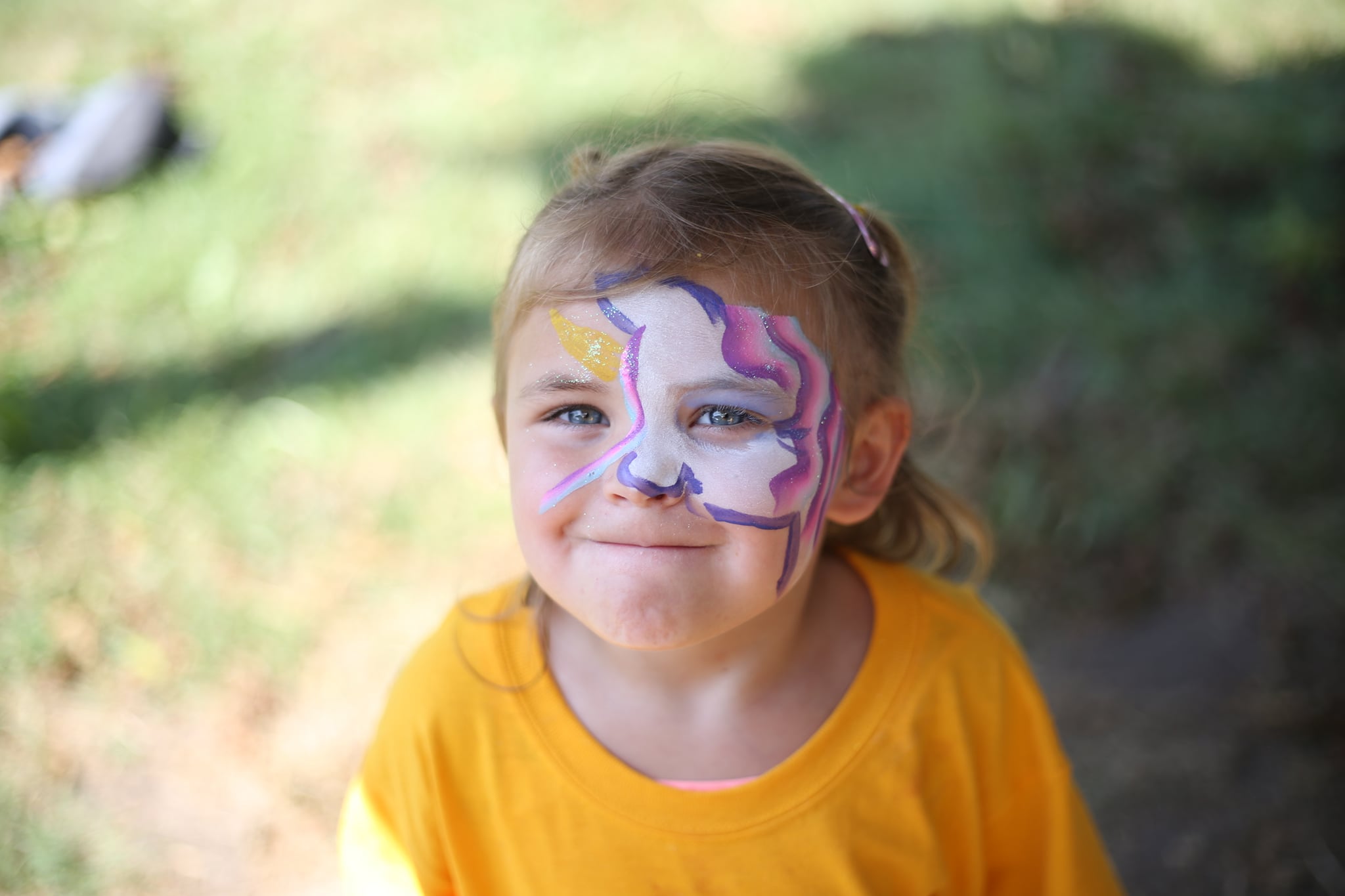 A little girl with unicorn facepaint smiles for the camera