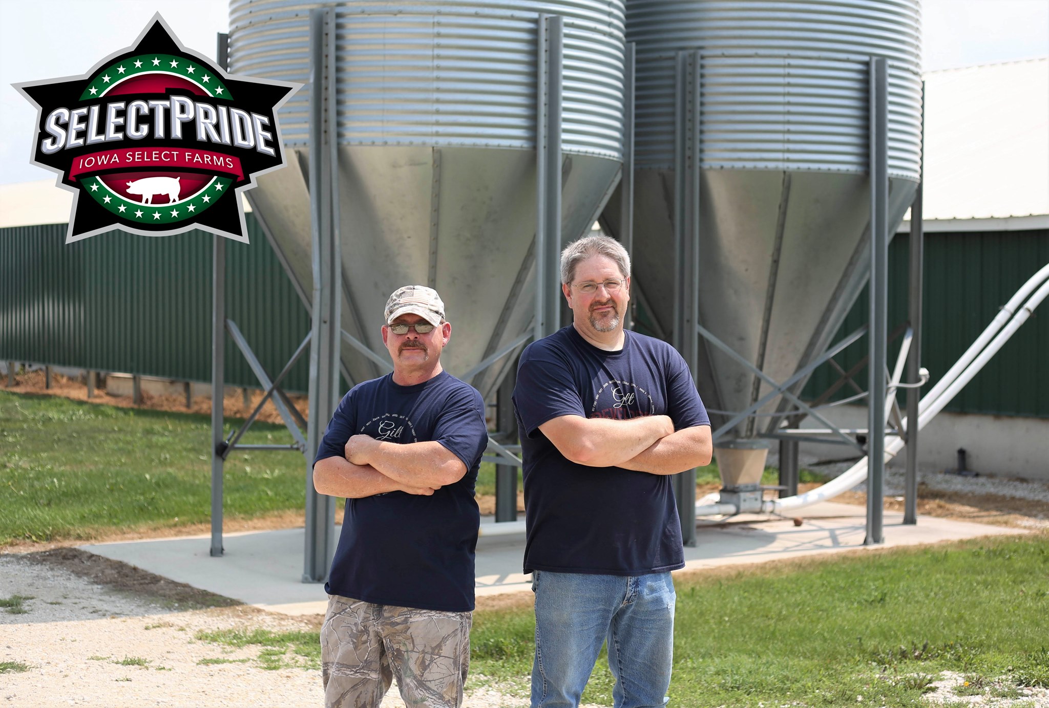 Two farmers pose in front of a pig feeder outdoors.