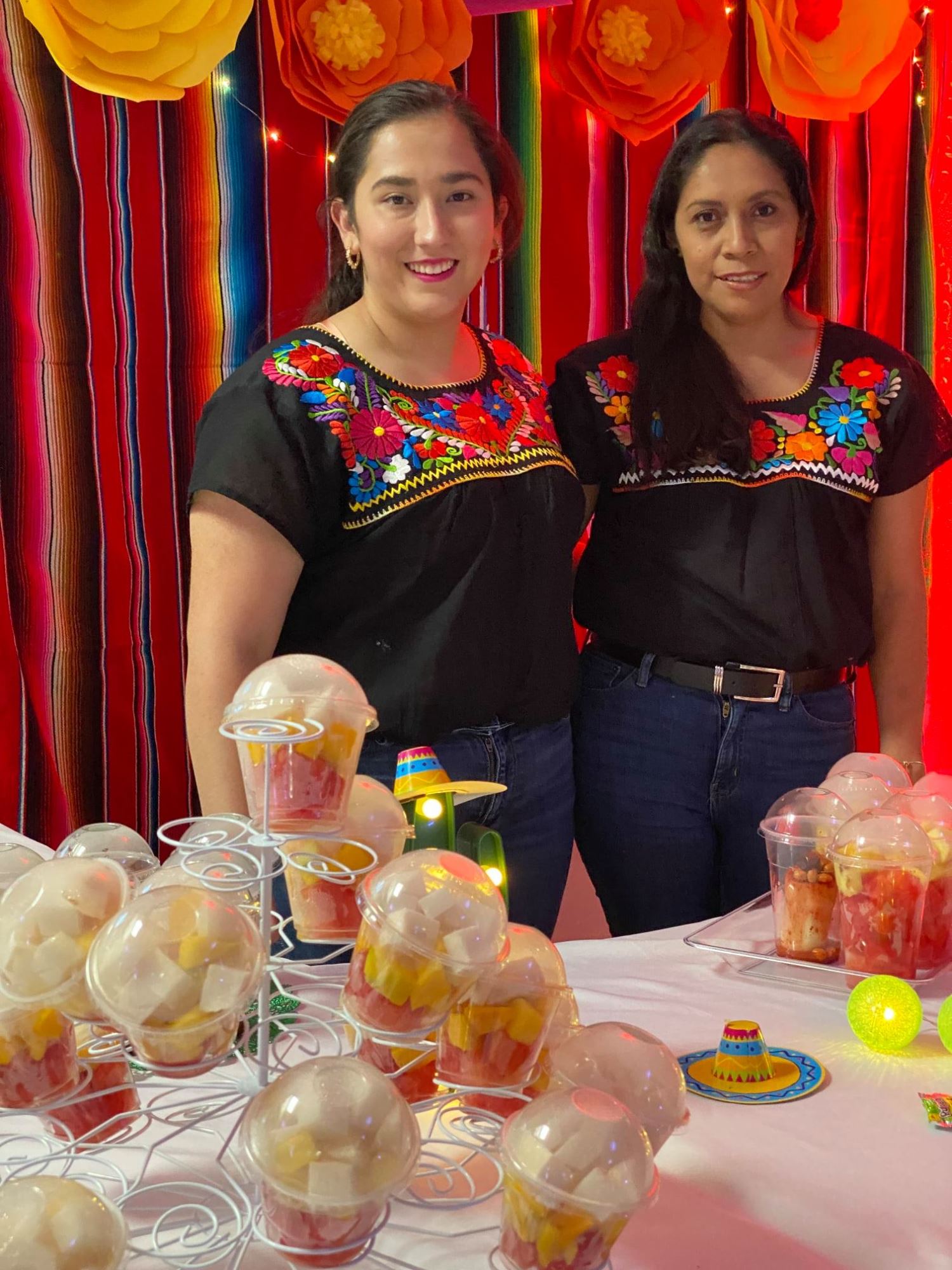 Two women pose with food in front of a festive background