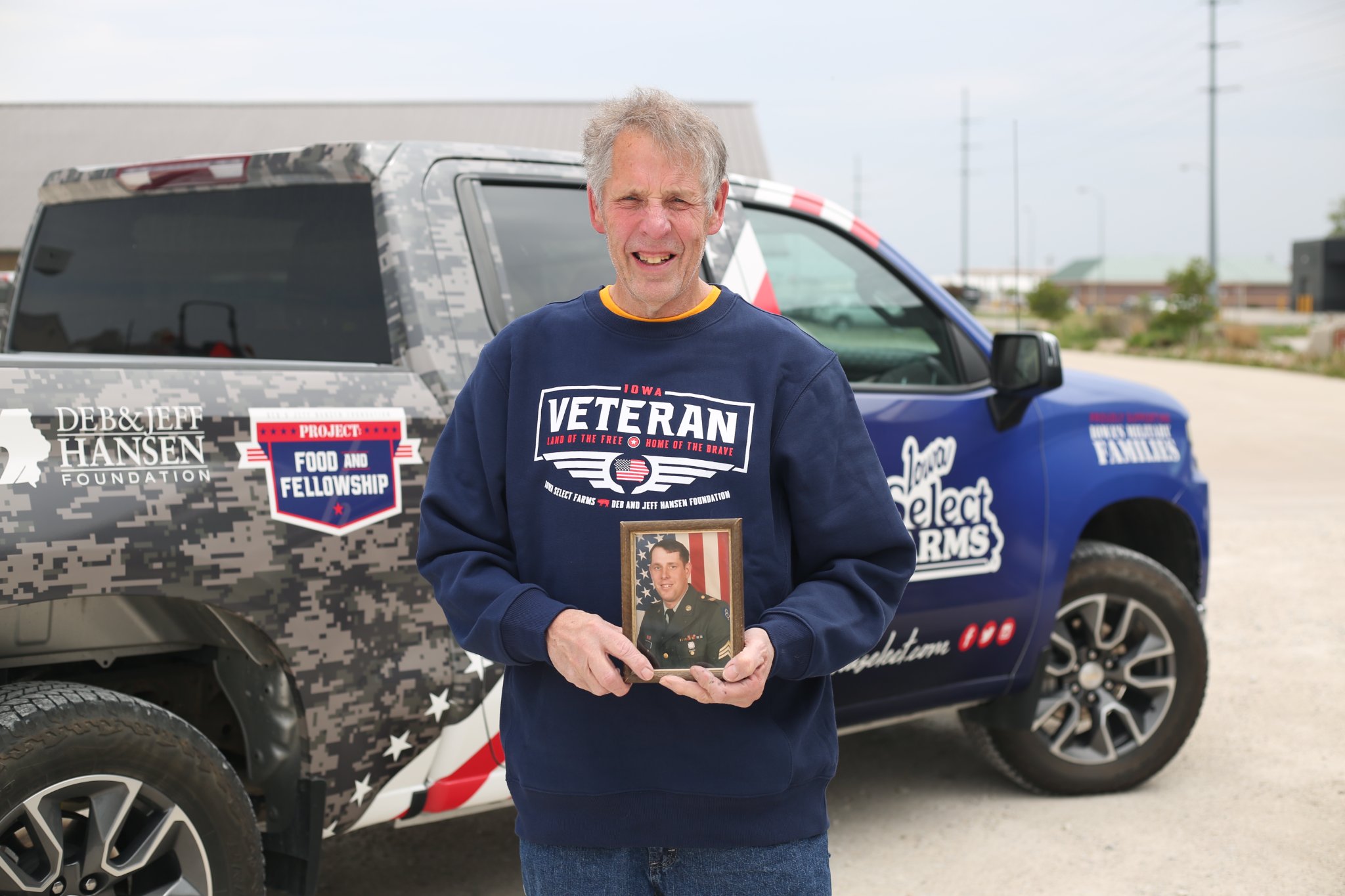 Randy holding a picture of himself while active duty by the truck