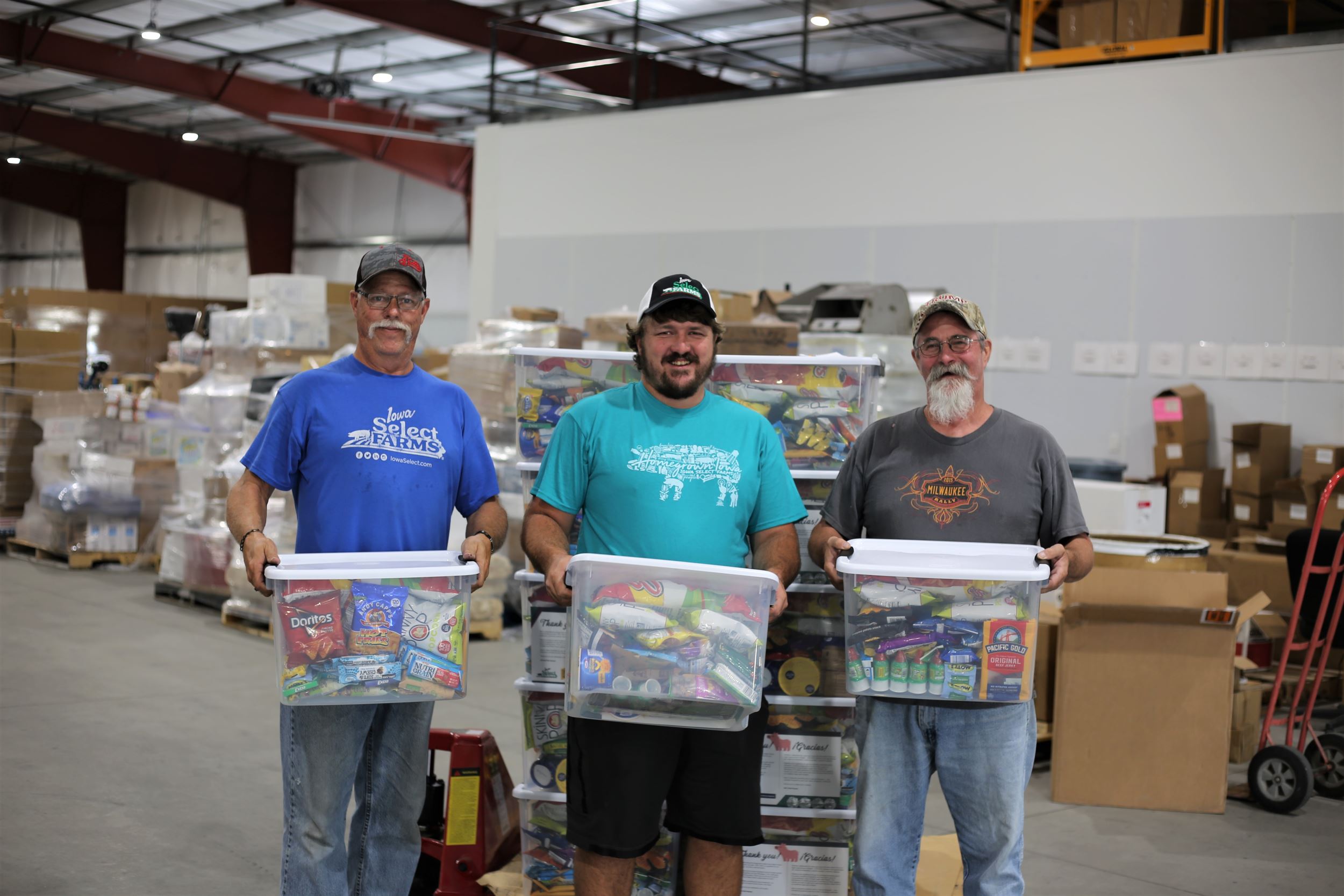 Three men stand holding the snack boxes in a warehouse.