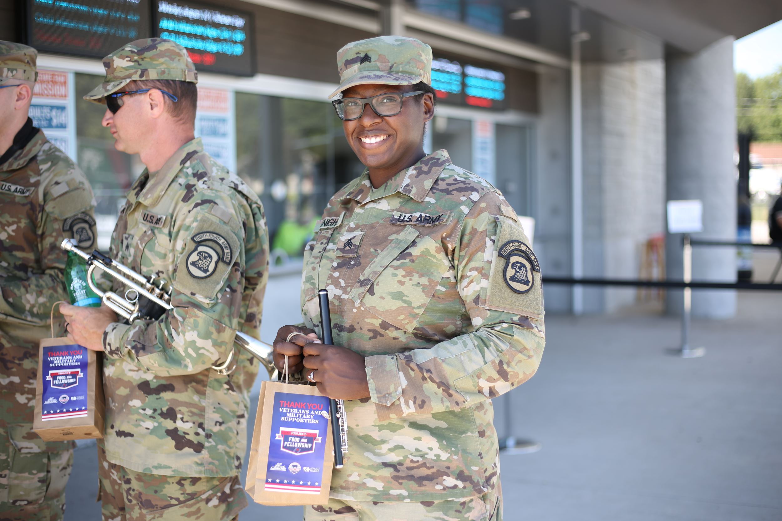 Military member in full uniform poses with a bag of food.