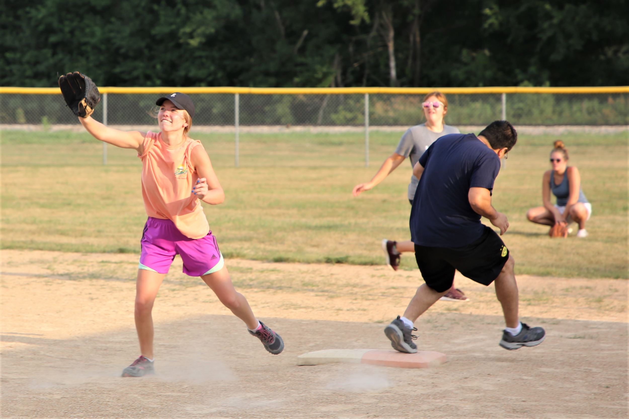 The first baseman tries to catch a ball and get an out but the runner is clearly too fast.