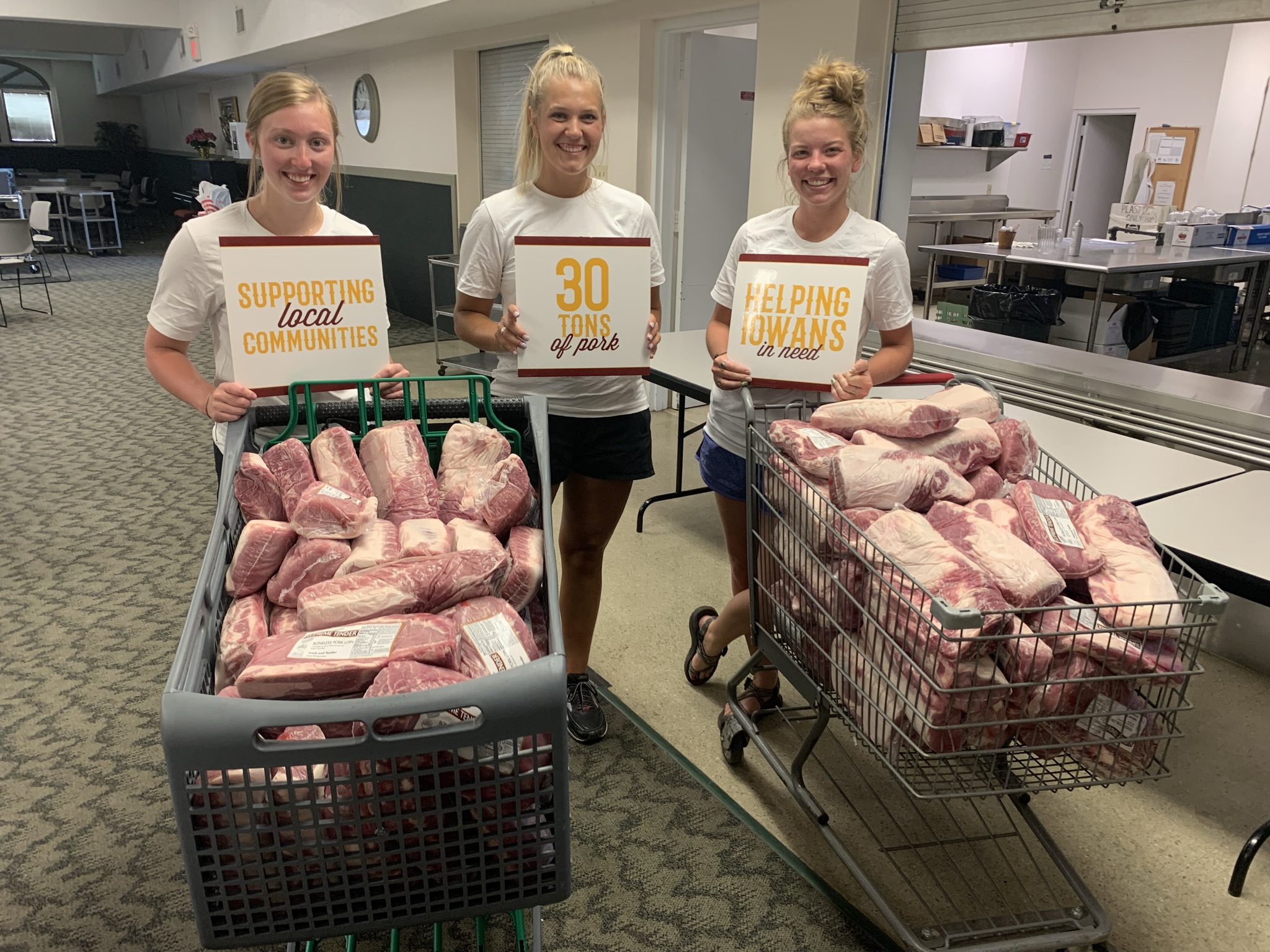 Three girls push two shopping carts full of pork.