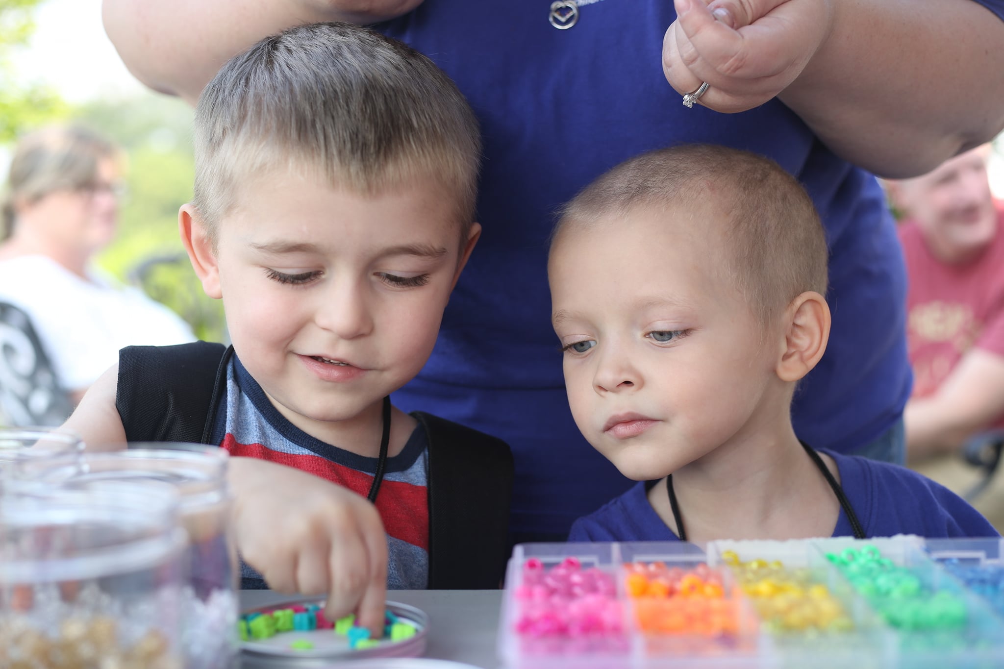 Two young boys look through a carton of colorful beads for their craft projects.